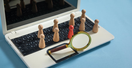 Magnifying glass, wooden human figures on laptop keyboard. Candidate selectionの写真素材