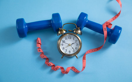 Measuring tape, alarm clock and dumbbells on the blue background.