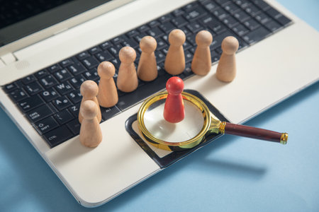 Magnifying glass, wooden human figures on laptop keyboard. Candidate selectionの写真素材
