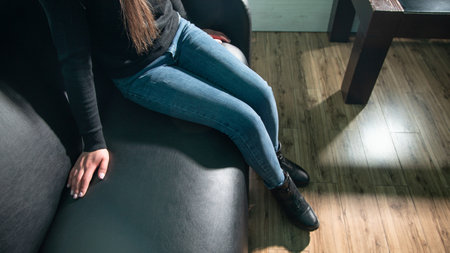 Woman sitting on black leather couch at home.の写真素材