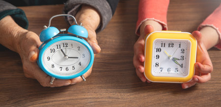 Hands of elderly female and young girl holding clock.の写真素材