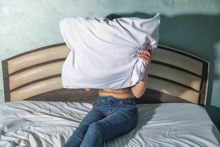 Caucasian young woman holding pillow on a bed.の写真素材
