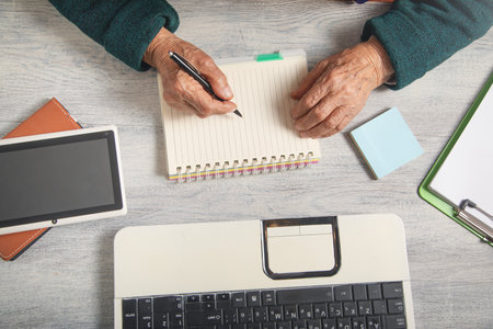 Caucasian elderly woman writes in notepad.