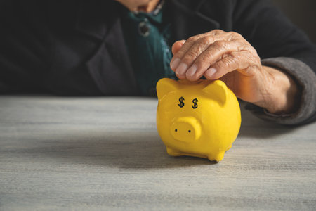 Elderly woman holding a piggy bank on the table.の写真素材