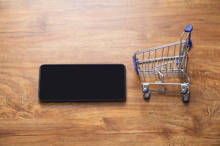 Shopping cart with a smartphone on the wooden table.の写真素材