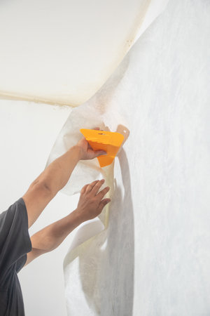 Caucasian worker applying wallpaper to wall at home.の写真素材