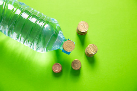 Plastic water bottle and coins on the green background.の写真素材