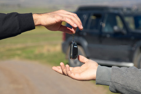 Man giving a car key to a woman on a rural road.