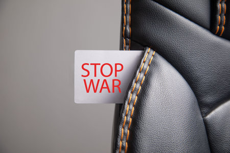 Stop war text on white paper label on leather car seat background.