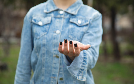 Woman with black nail polish on the palm of her hand, outdoors