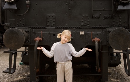 Small blonde girl spreads her hands in front of an old locomotive の写真素材