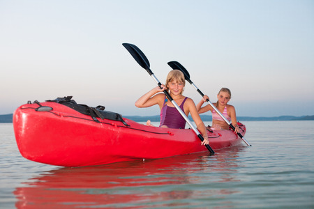 Girls with paddle and kayak on a lake at sunsetの写真素材
