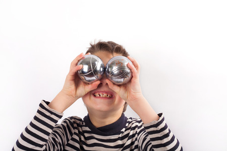 Naughty boy holding petanque balls in front of his eyes. Isolated on white.