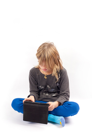 Young girl sitting cross-legged using a tablet. Studio shot isolated on white.の写真素材