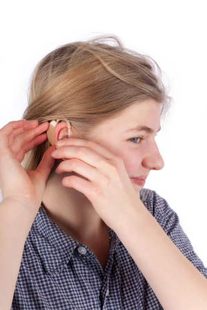 Girl inserting her hearing aid into her ear. Studio isolated on white background.の写真素材