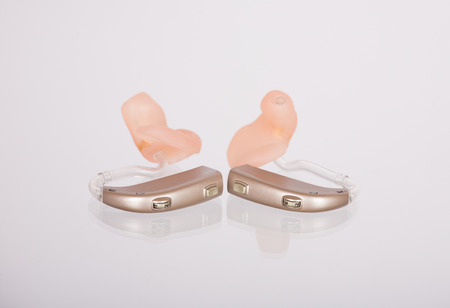 Two hearing aids left and right with ear moulds on a mirroring glass surface