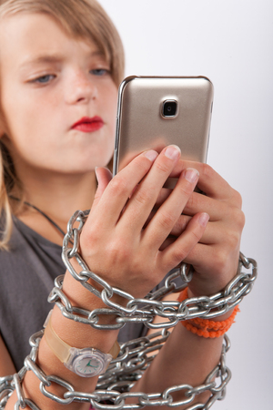 Mobile addiction - Young girl shackled with a chain using smartphoneの写真素材
