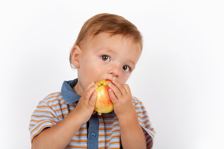 Cute baby boy eating apple. Isolated on white background.の写真素材