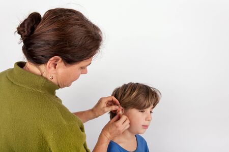Woman audiologist fitting a young boy with  hearing aid
