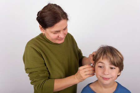 Mother inserting a hearing aid into her sons earの写真素材