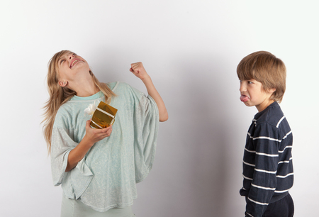 Happy girl with gift and an angry boy streching out her tongueの写真素材