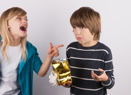Boy got a simple mobile phone in a gift box, his sister laughing on himの写真素材