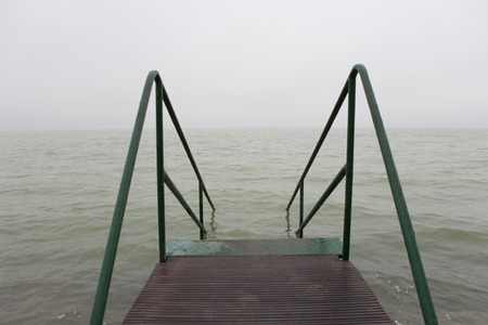 Bad weather over a lake with a gray and characterless sky and with a pier stairs to the lake.の写真素材