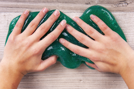 Young girlâs hands squeezing green slime on a wooden tableの写真素材