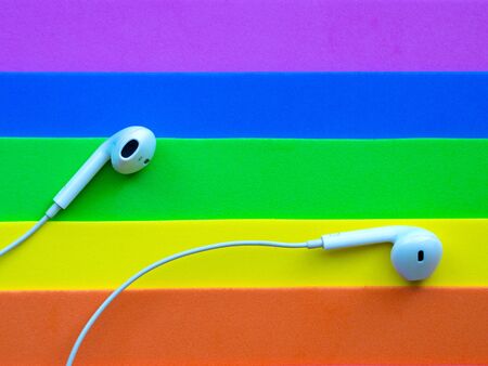 White wired headphones, headset on a multi-colored rainbow background (lgbt). Musical day