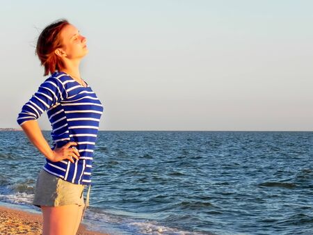 young woman in a striped t-shirt on the sea enjoying the sunsetの写真素材