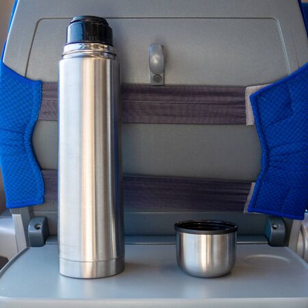 A metal thermos with a coffee mug on a folding table in a trainの写真素材