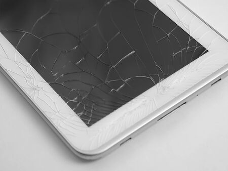 Broken electronic device isolated on wooden background. Broken tablet touch screenの写真素材