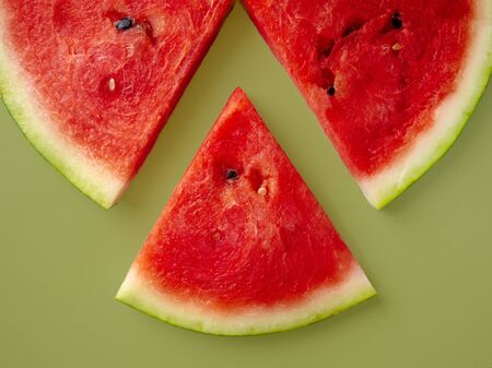 Slices of fresh red delicious watermelon are laid out in a circle on a colored background.