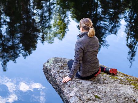 Woman sitting on a rocky ledge above the cloudsの写真素材