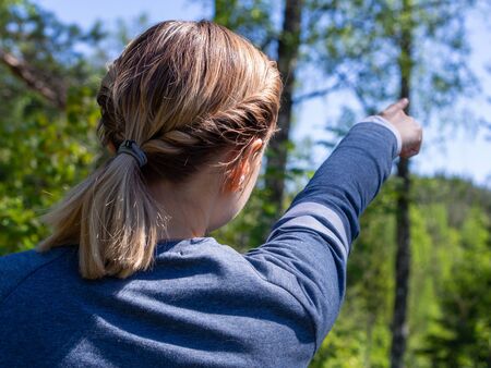 Woman shows direction in the forest. View from the backの写真素材