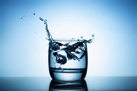 Ice cubes splashing into glass of water.の写真素材
