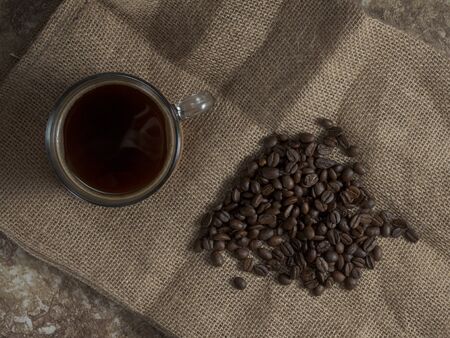 dark roasted coffee beans on burlap and a mug of freshly brewed natural coffee.の写真素材