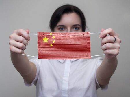 Woman holds out a medical mask with the image of the flag of China. Coronavirus COVID-19の写真素材