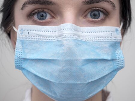 Portrait of a young European woman in a protective disposable medical mask. Concept of caronavirus Cavid 19 and human quarantine. Girl in a mask on a white wall. Masked medical workerの写真素材