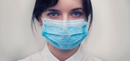 Portrait of a young European woman in a protective disposable medical mask. Concept of caronavirus Cavid 19 and human quarantine. Girl in a mask on a white wall. Masked medical workerの写真素材