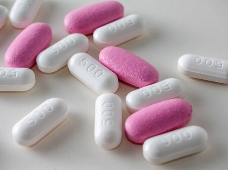 multicolored medical pills and packs of pills on a white table.