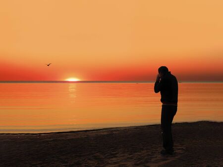 Back view of a silhouette of a man photographing the sun at sunset on the beach on holidays.の写真素材