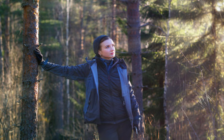 Happy woman hiker leaned against a tree in a sunny forestの写真素材