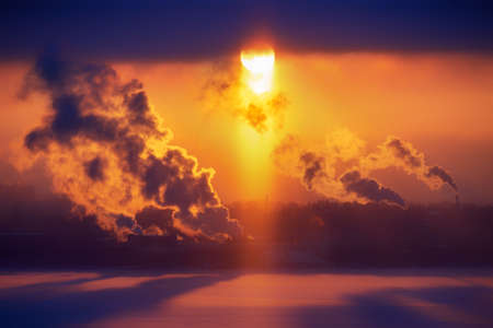 Chimneys of a factory with smoke and steam on a red sunset in the backgroundの写真素材