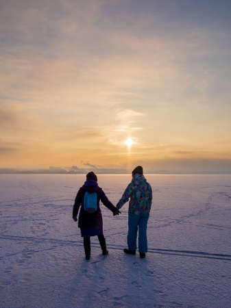 Two girls go into the sunset along the frozen riverの写真素材
