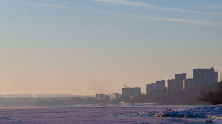 Coast of the winter river in Siberia. Skyline with outlines of houses and steam above the waterの写真素材
