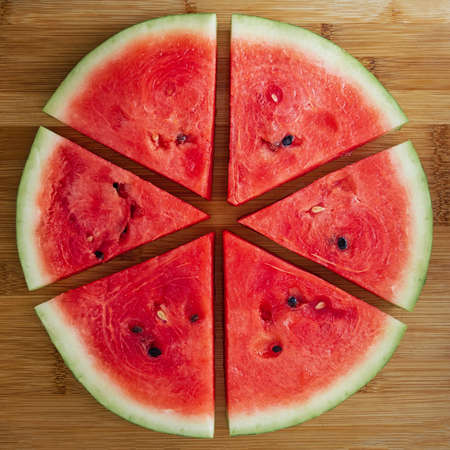 Slices of fresh red tasty watermelon laid out in a circle on a wooden background.の写真素材