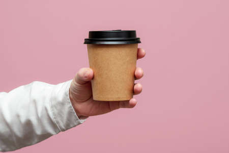 Woman hands hold paper cup on pink background. Copy space.の写真素材