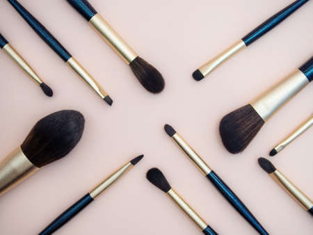 Assortment of female make-up of various face brushes. A set of professional dark blue and golden makeup brushes on a pink background. photoの写真素材