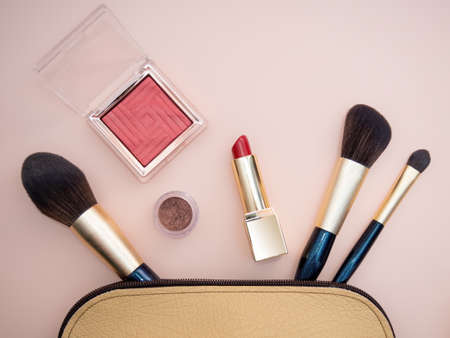 Top view of cosmetics standing out from beige makeup bag on pink background. photoの写真素材